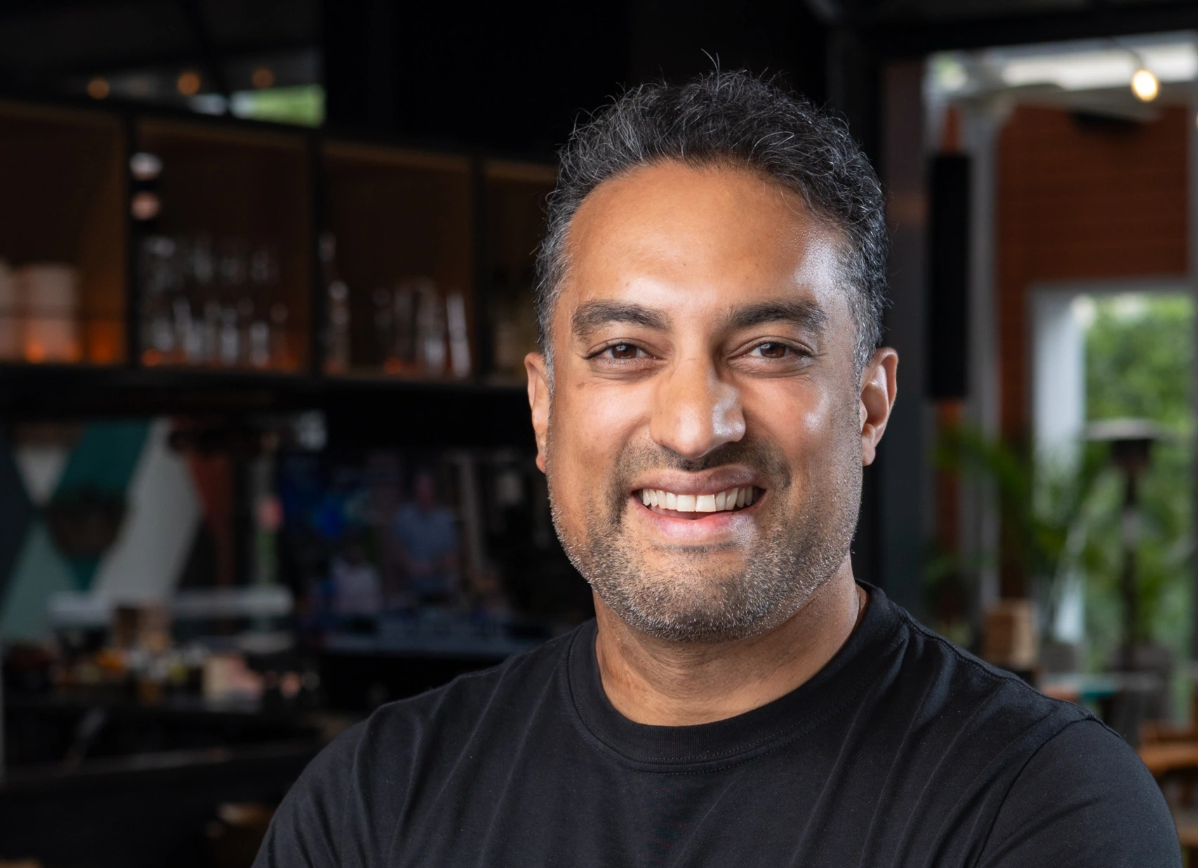 Smiling man in a black shirt with arms crossed in a cafe - Opus1: Everything You Need to Run Your School in One Place