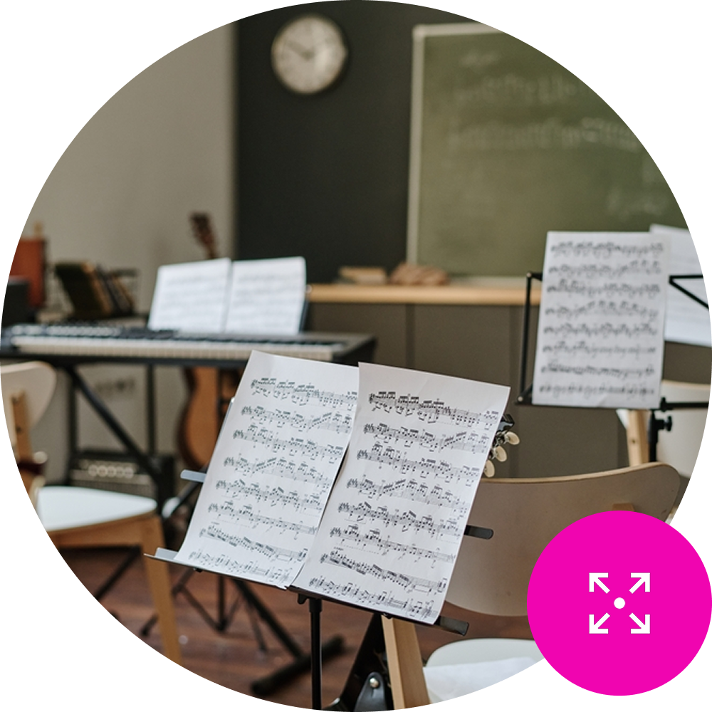 Sheet music on a stand in an empty music classroom - Resource Management Icon in the bottom right on brand pink background