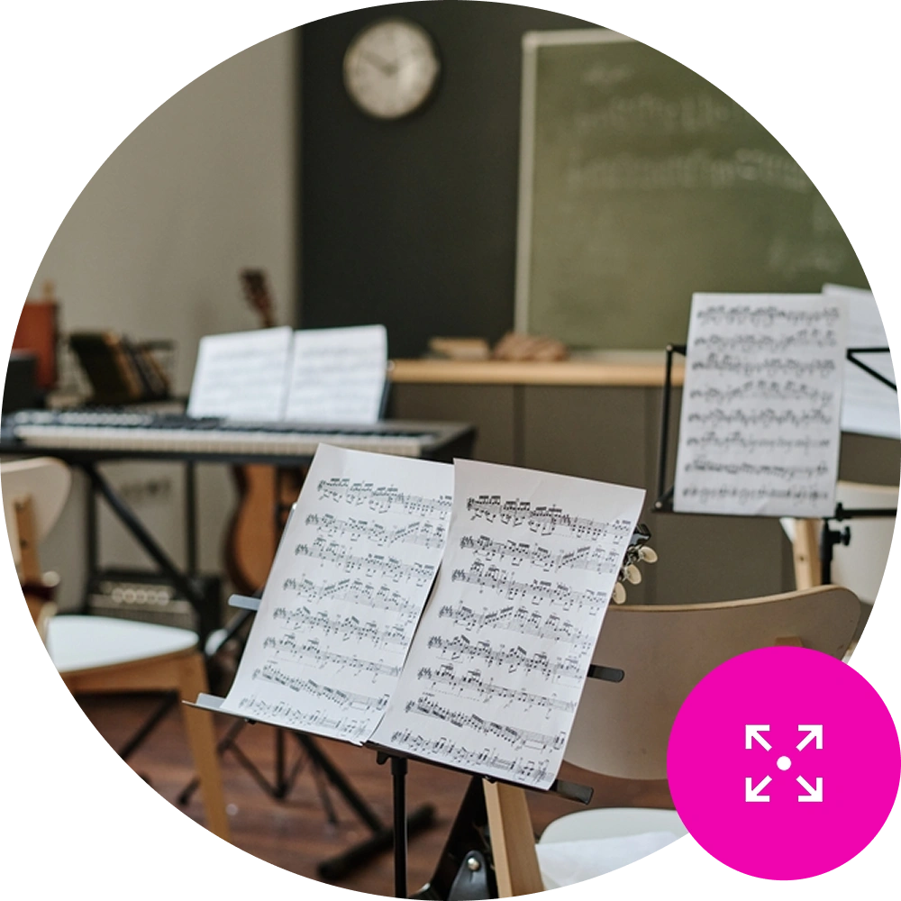 Sheet music on a stand in an empty music classroom - Resource Management Icon in the bottom right on brand pink background