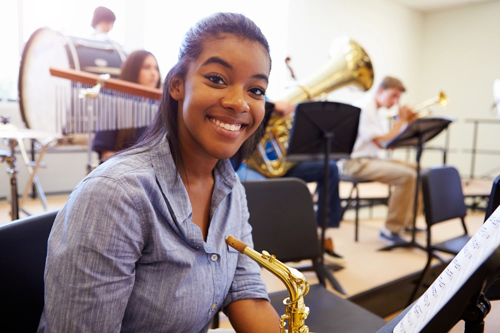 Highschool girl smiling at the cameron while sitting in band class with her saxophone