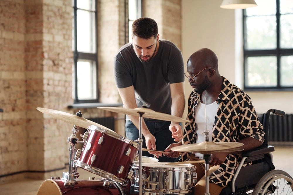 A drum instructor works closely with an adult student in a wheelchair during an adaptive one-on-one percussion lesson.