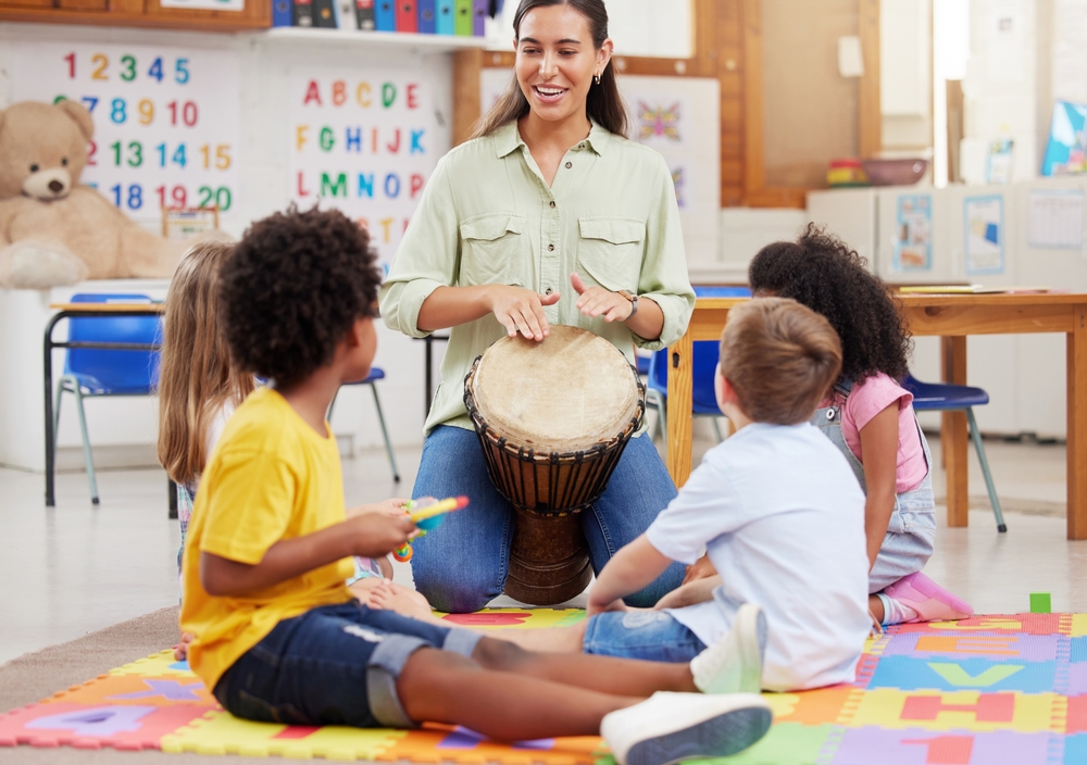 A preschool music teacher leads a fun and interactive drumming circle with young children in a colorful classroom.