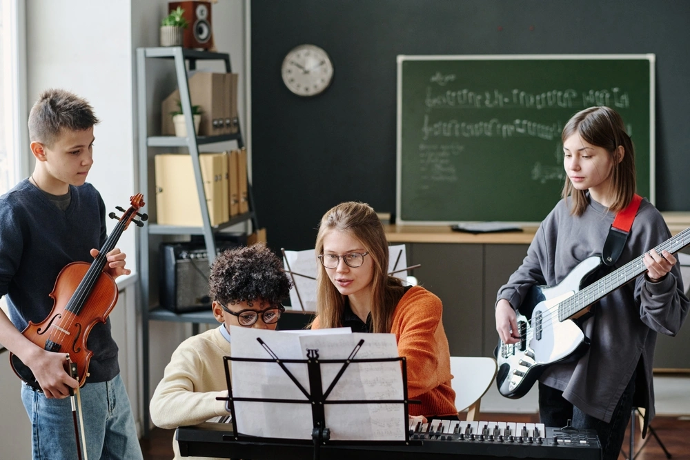 Woman sitting at piano teaching three kids, two of them standing next to her and the other sitting on the bench