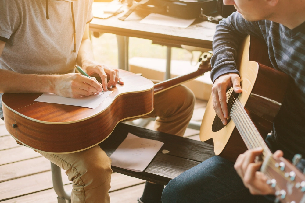 Two guitar students collaborate on songwriting, jotting down notes while practicing together during a music lesson.