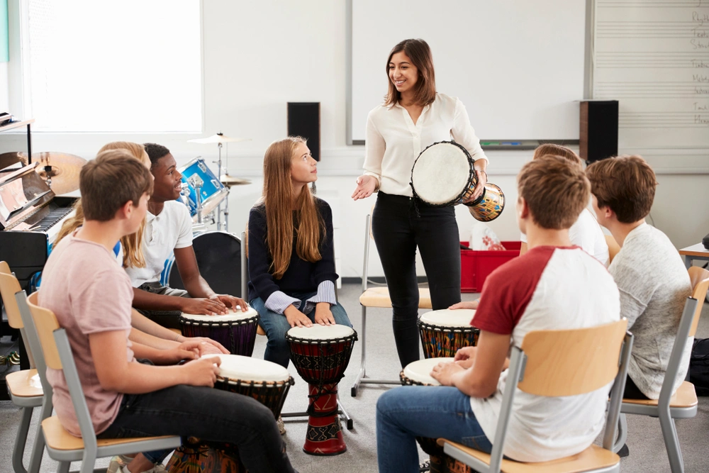 A music teacher leads a group of students in a rhythm-based drumming activity during a classroom percussion lesson.