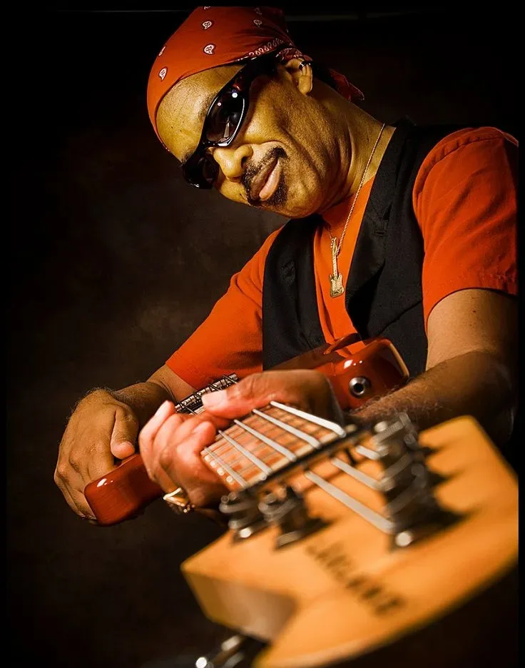Jon Gee with guitar and sunglasses looking at the camera