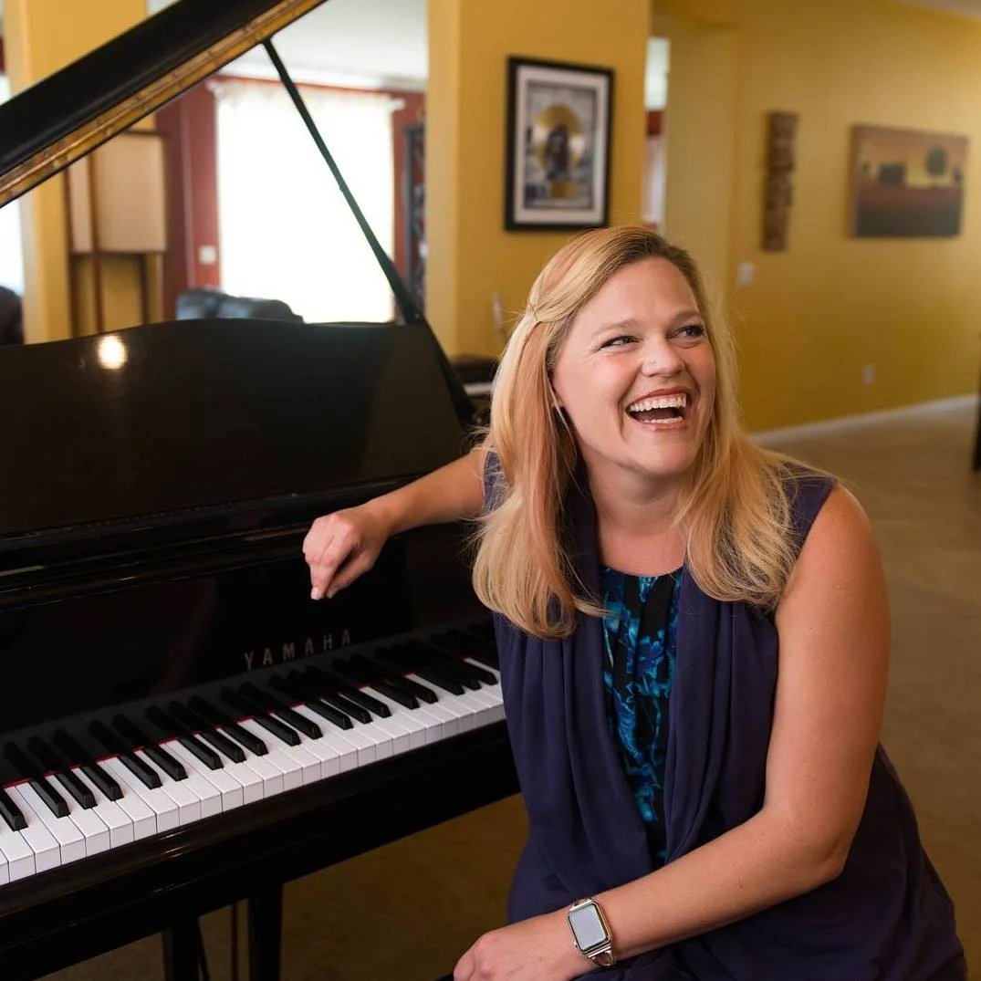 Ruthie Smith - Music Teacher - sitting at piano and smiling at something off camera