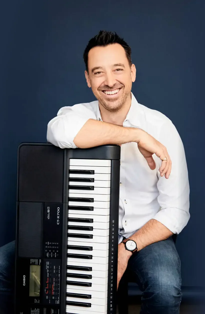 Tim Topham sitting with keyboard on blue background