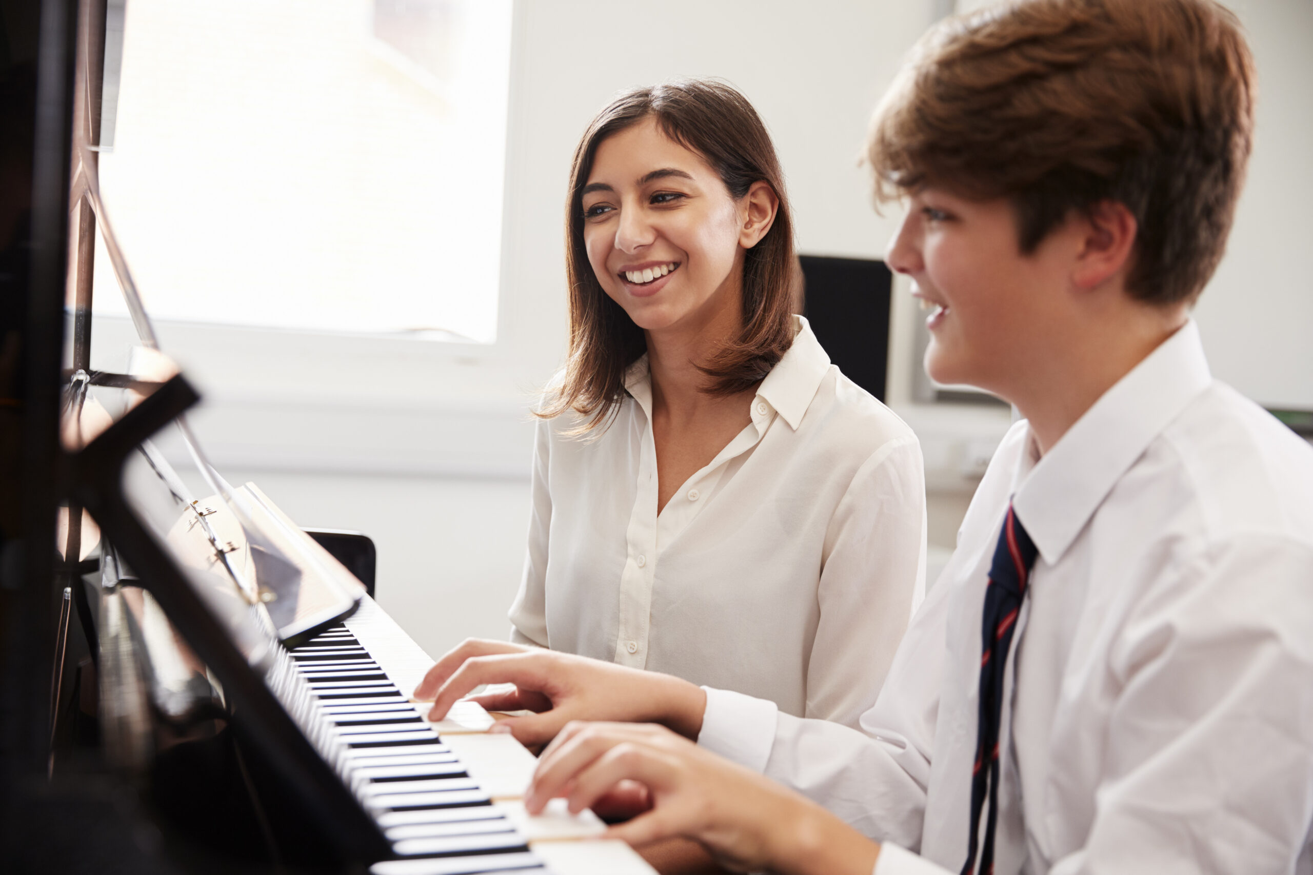 Male student plays piano next to a female teacher in a music lesson