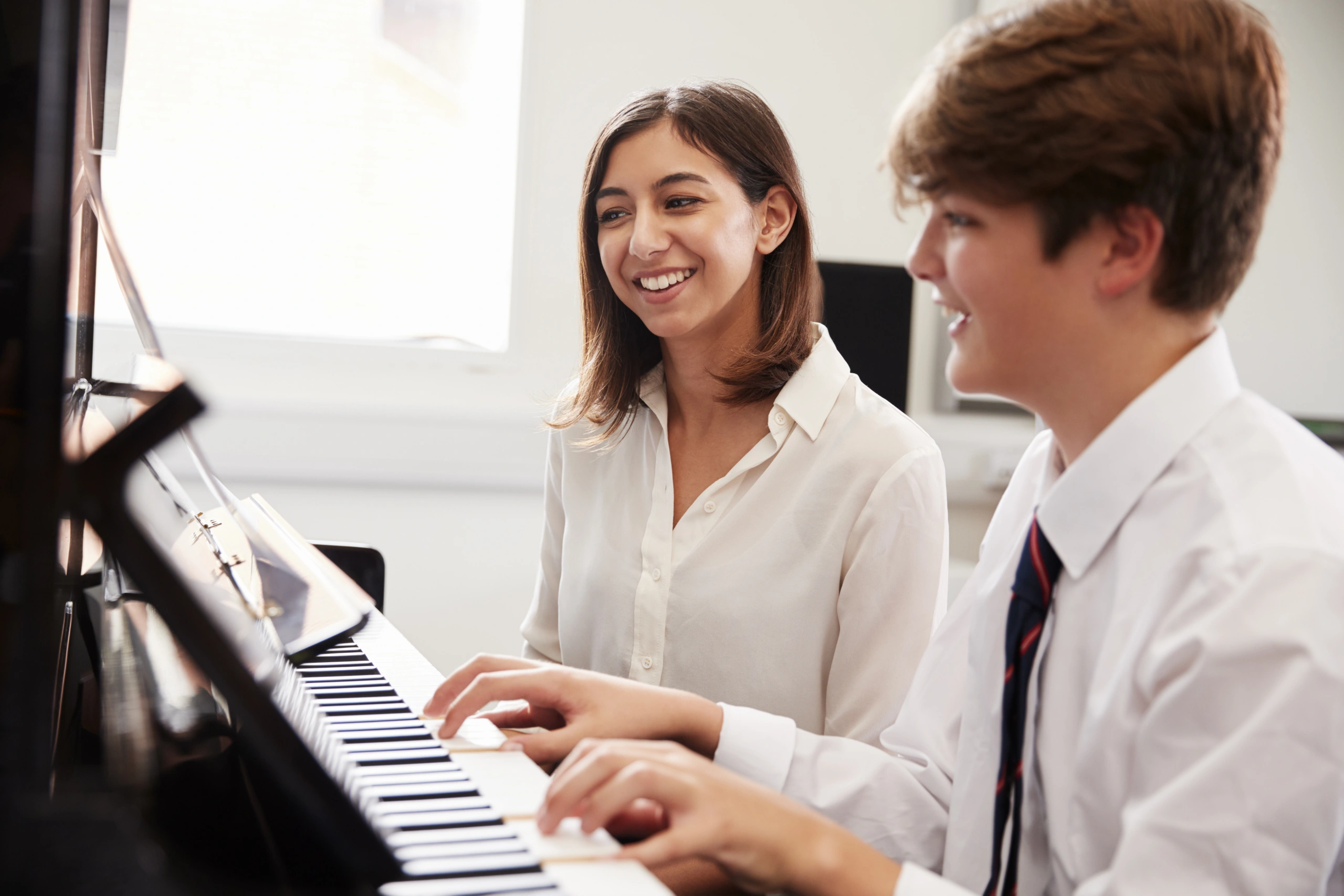 Male student plays piano next to a female teacher in a music lesson