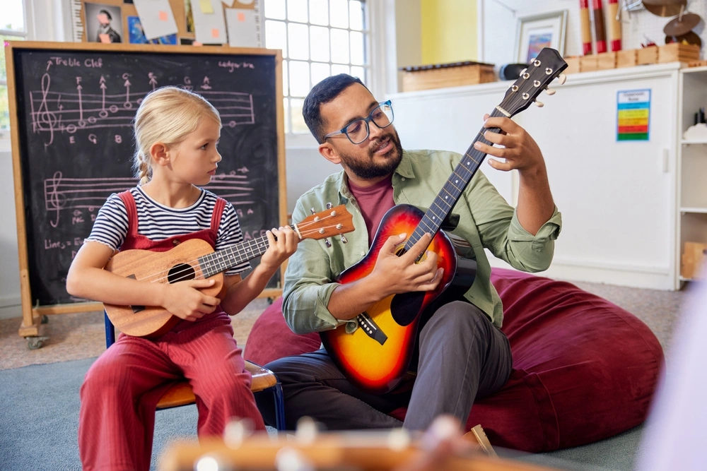 A teacher showing a girl a chord on guitar.