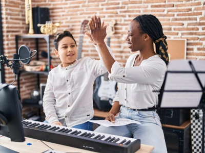 Young piano student high fiving teacher in front of piano during a lesson