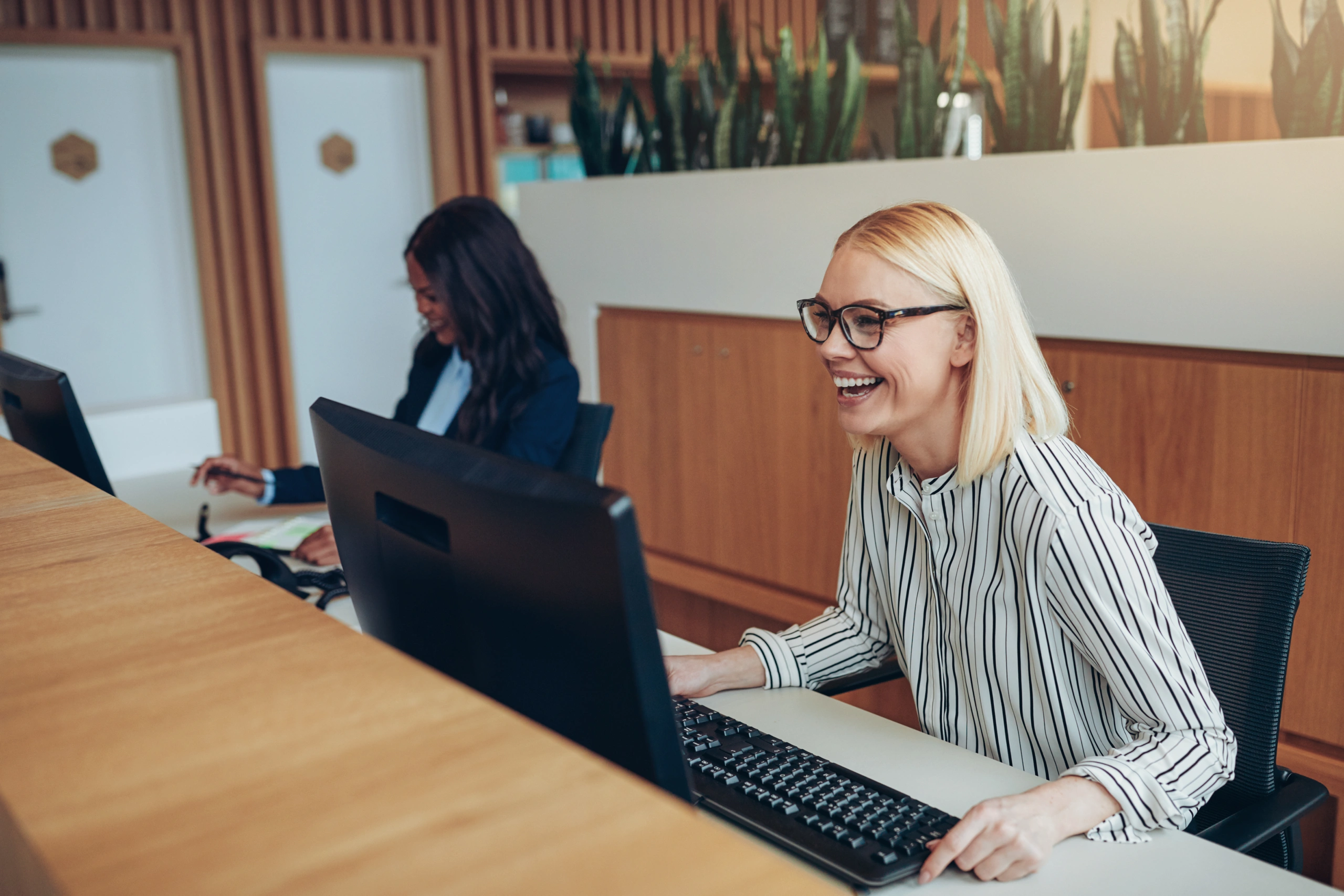 Receptionists laughing and working at desks in a modern office setting - Opus1: Everything You Need to Run Your School in One Place