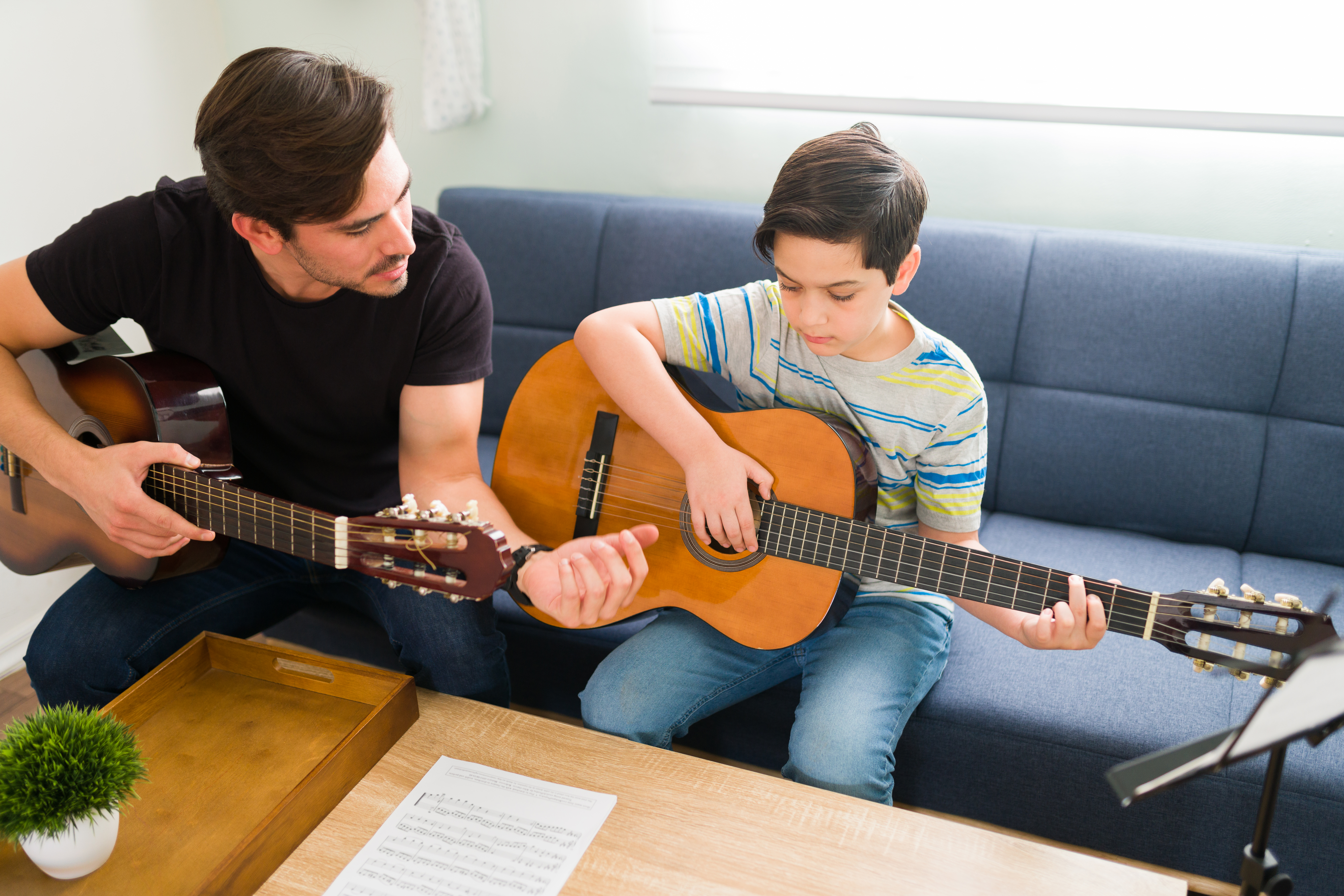 Father teaching son to play guitar in living room - Opus1: Everything You Need to Run Your School in One Place